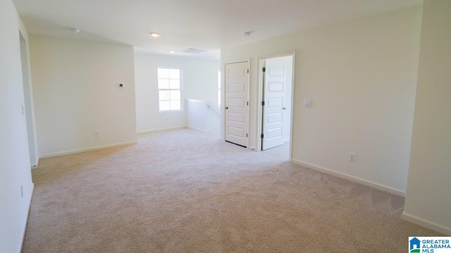 empty room featuring light carpet, visible vents, and baseboards