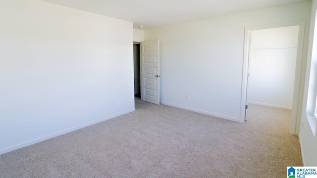 unfurnished bedroom with a walk in closet, a closet, baseboards, and carpet floors