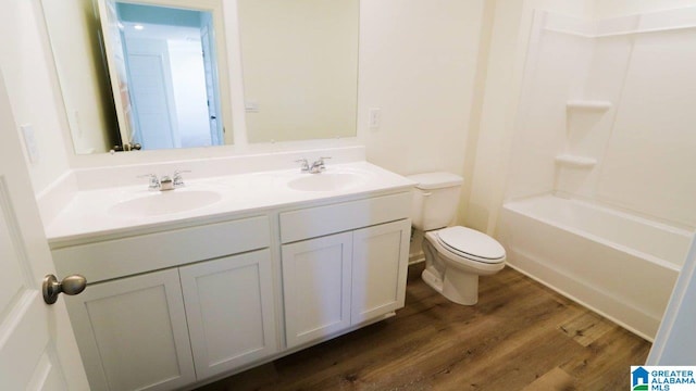 bathroom with double vanity, wood finished floors, toilet, and a sink