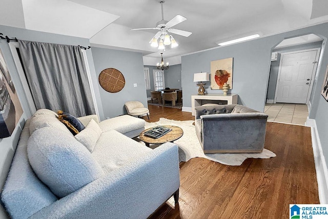 living room featuring wood finished floors, a ceiling fan, baseboards, arched walkways, and crown molding