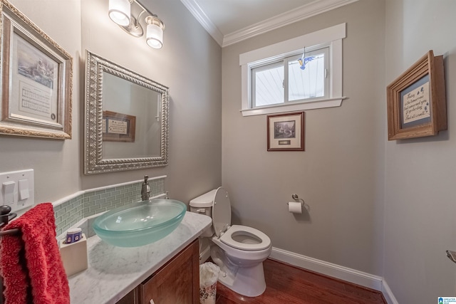 bathroom featuring vanity, wood finished floors, baseboards, crown molding, and toilet