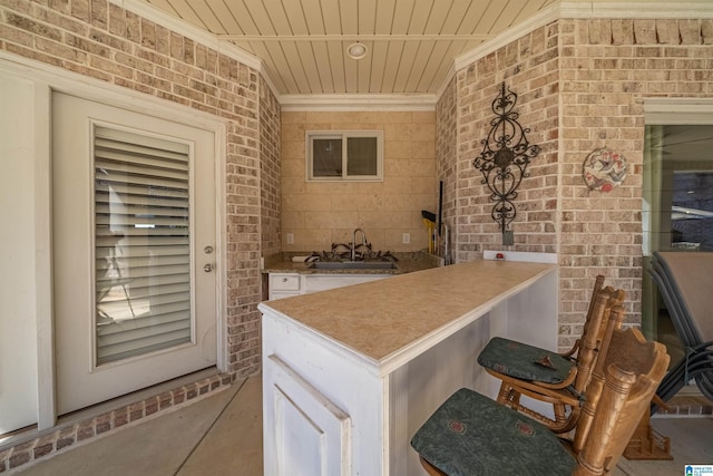 kitchen featuring brick wall, crown molding, wood ceiling, white cabinetry, and a sink