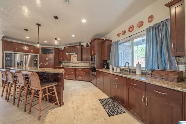 kitchen with backsplash, under cabinet range hood, a kitchen bar, stainless steel appliances, and a sink