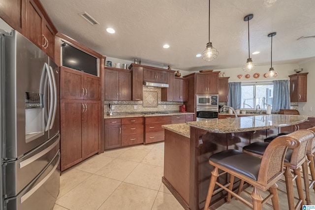 kitchen featuring visible vents, a breakfast bar, under cabinet range hood, backsplash, and stainless steel appliances