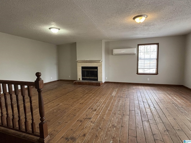 unfurnished living room with a glass covered fireplace, an AC wall unit, dark wood-type flooring, and baseboards