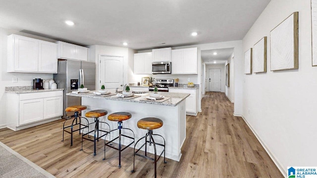 kitchen featuring a breakfast bar, an island with sink, light wood-type flooring, appliances with stainless steel finishes, and white cabinets