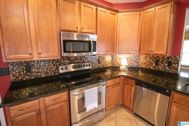 kitchen with decorative backsplash, dark stone countertops, light tile patterned floors, and appliances with stainless steel finishes