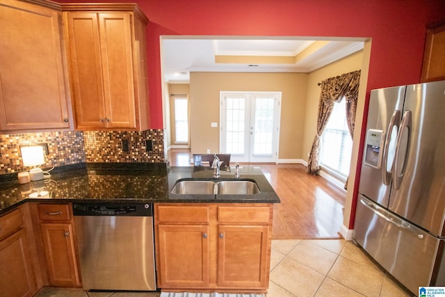 kitchen with crown molding, dark stone counters, appliances with stainless steel finishes, a raised ceiling, and a sink