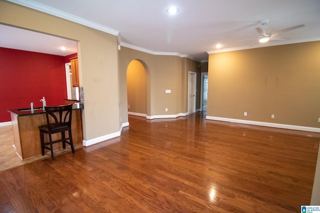 unfurnished living room with wood finished floors, baseboards, arched walkways, ornamental molding, and ceiling fan