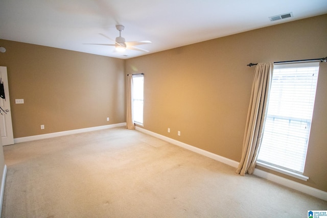 spare room with light colored carpet, a ceiling fan, visible vents, and baseboards