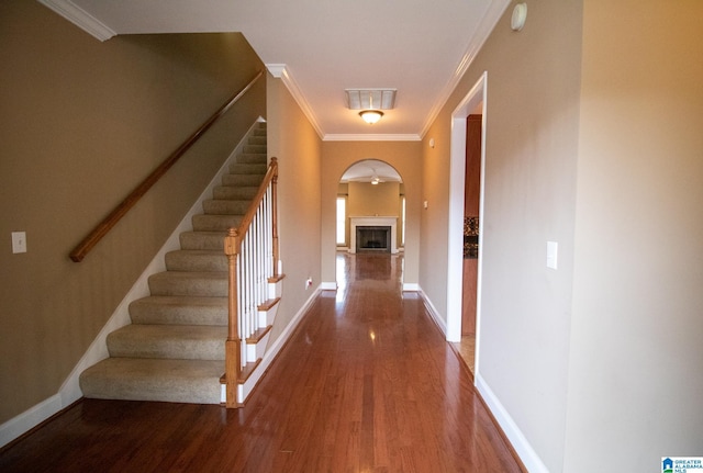 hallway featuring stairway, arched walkways, wood finished floors, and ornamental molding