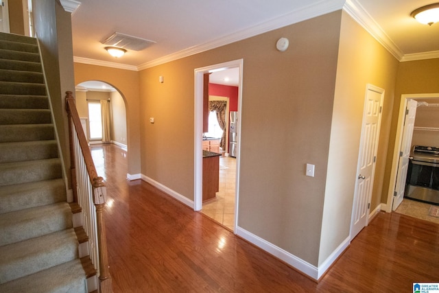 corridor with stairway, baseboards, light wood finished floors, arched walkways, and crown molding