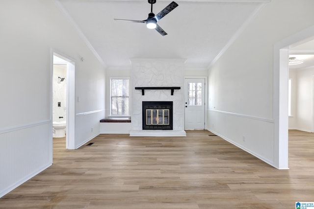 unfurnished living room with a large fireplace, plenty of natural light, ornamental molding, and a ceiling fan