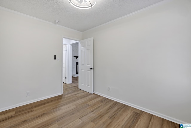 empty room with light wood-type flooring, baseboards, a textured ceiling, and crown molding