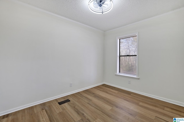 unfurnished room featuring visible vents, a textured ceiling, wood finished floors, crown molding, and baseboards