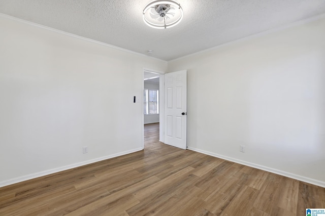 spare room featuring baseboards, a textured ceiling, wood finished floors, and ornamental molding