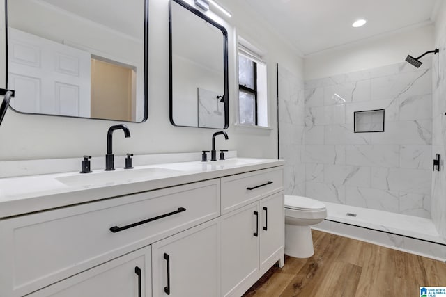 bathroom with wood finished floors, double vanity, a tile shower, a sink, and toilet