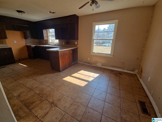 kitchen with visible vents, a ceiling fan, a peninsula, light countertops, and light tile patterned floors