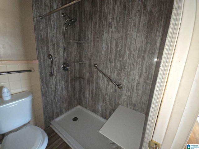 full bathroom with tile walls, toilet, a tile shower, and wainscoting