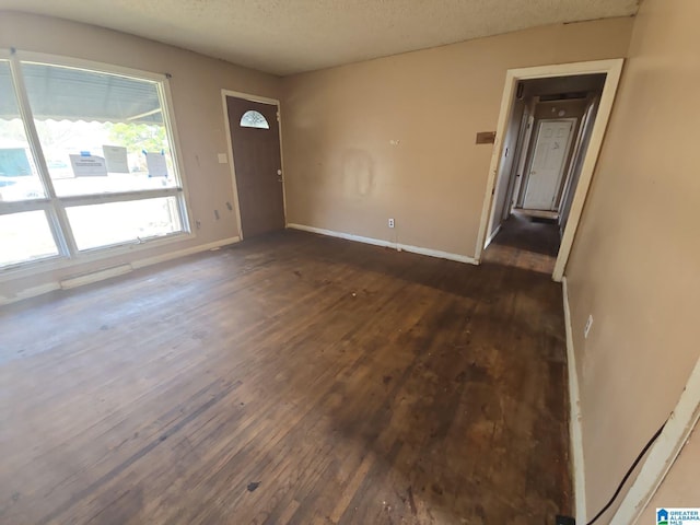 unfurnished room with dark wood-style floors, a textured ceiling, and baseboards