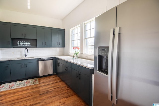 kitchen featuring backsplash, dark wood-type flooring, light stone countertops, stainless steel appliances, and a sink