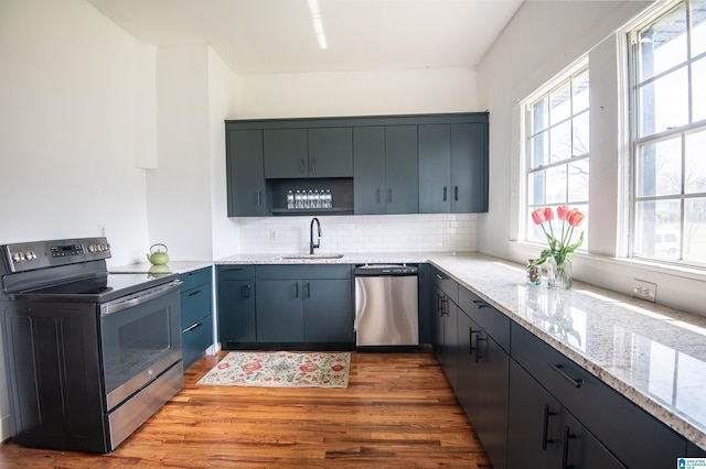 kitchen featuring a sink, light stone counters, tasteful backsplash, wood finished floors, and appliances with stainless steel finishes