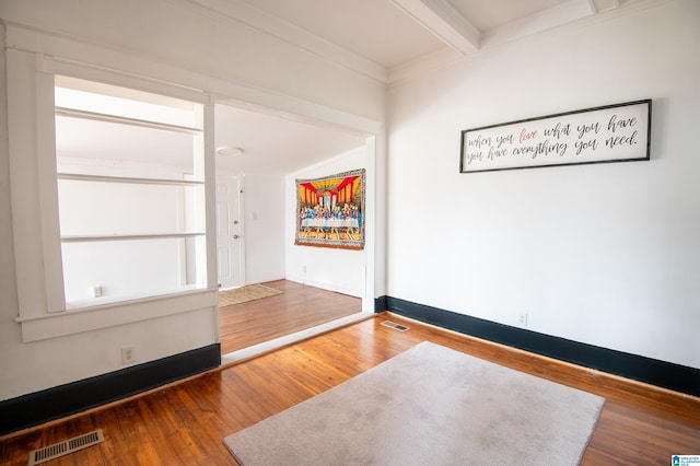 spare room featuring visible vents, beamed ceiling, baseboards, and hardwood / wood-style floors