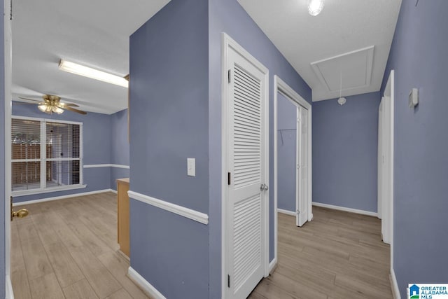 hallway featuring baseboards, attic access, and light wood finished floors