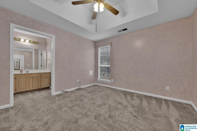 unfurnished bedroom with baseboards, visible vents, a tray ceiling, ensuite bathroom, and carpet flooring