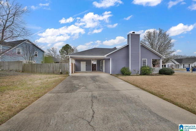 view of front of home featuring driveway, fence, a front yard, a carport, and a chimney