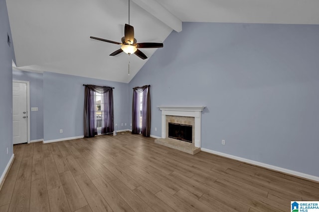 unfurnished living room featuring a fireplace with raised hearth, baseboards, beamed ceiling, wood finished floors, and a ceiling fan