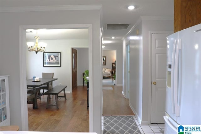 interior space featuring visible vents, light wood-style flooring, ornamental molding, white fridge with ice dispenser, and a chandelier