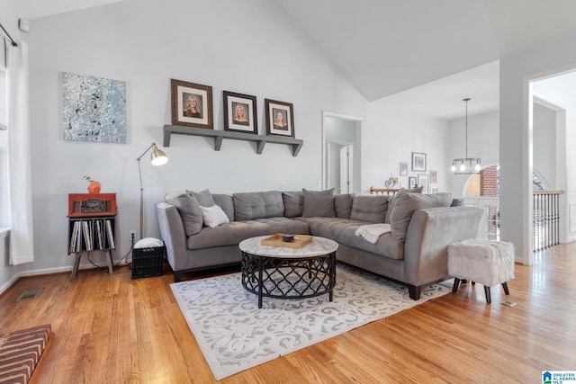 living area with visible vents, baseboards, an inviting chandelier, wood finished floors, and high vaulted ceiling