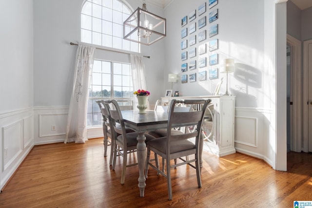 dining room with an inviting chandelier, a decorative wall, light wood-type flooring, and wainscoting