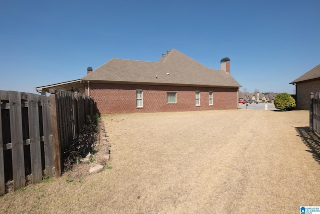 view of side of home featuring brick siding, a chimney, and fence