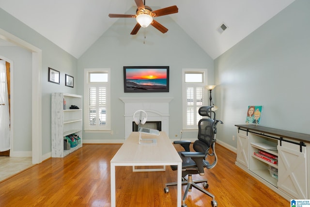 office area with visible vents, high vaulted ceiling, light wood-style flooring, a fireplace, and ceiling fan