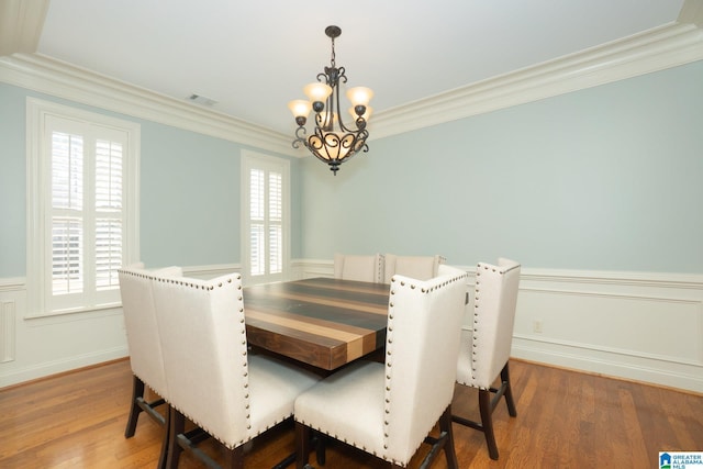 dining area with ornamental molding, a notable chandelier, wood finished floors, and wainscoting