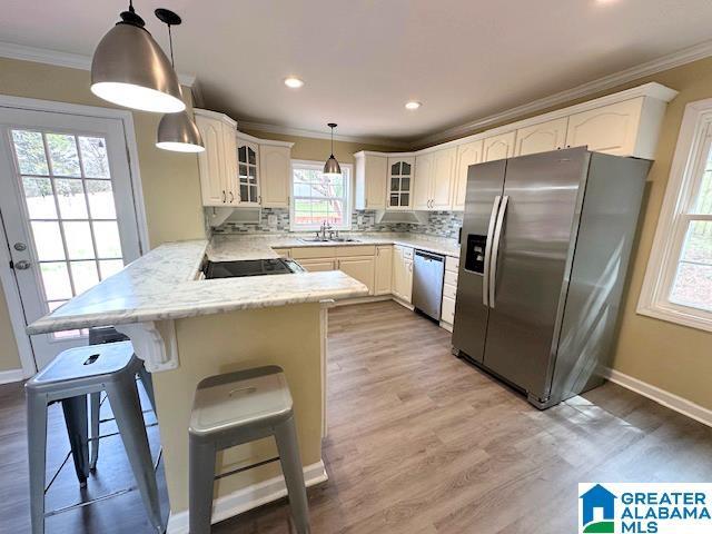 kitchen with crown molding, glass insert cabinets, appliances with stainless steel finishes, a peninsula, and a sink