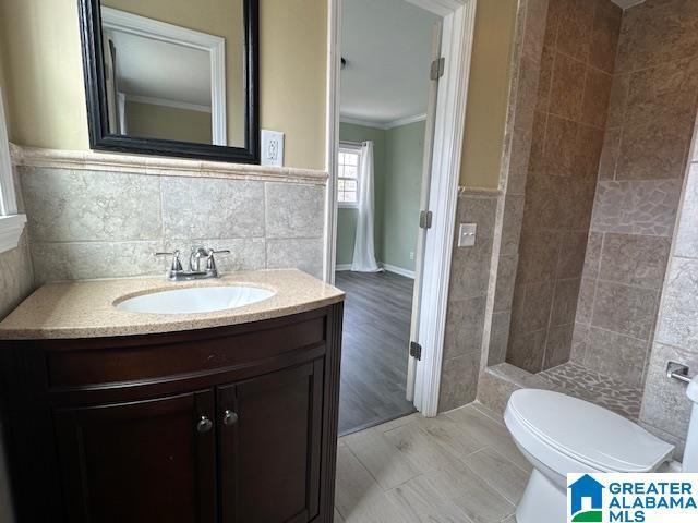 full bathroom with tile walls, ornamental molding, vanity, and a tile shower