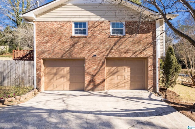 view of side of property with brick siding, driveway, a garage, and fence