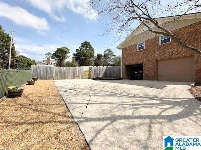 view of property exterior featuring brick siding, concrete driveway, a garage, and fence