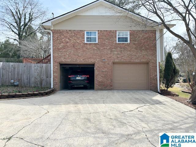 view of side of home with concrete driveway, an attached garage, fence, and brick siding