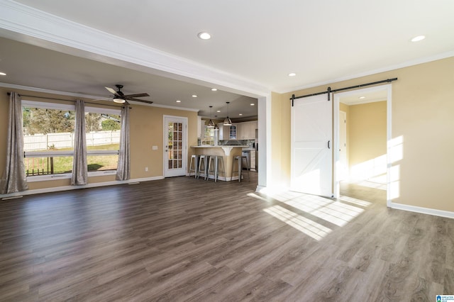 unfurnished living room with a barn door, dark wood-style floors, baseboards, and ornamental molding