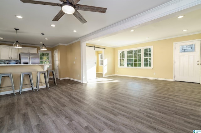 unfurnished living room with ceiling fan, a barn door, dark wood-type flooring, and ornamental molding