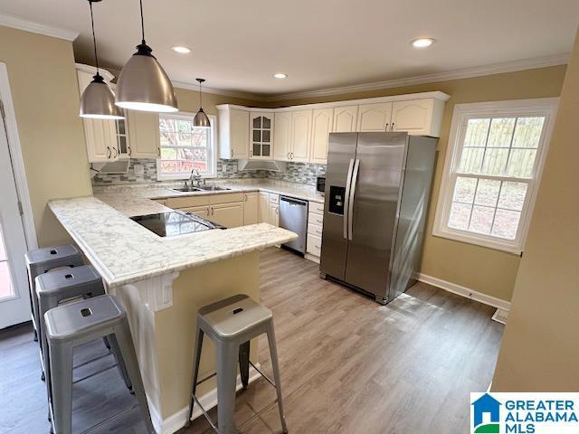 kitchen with a peninsula, glass insert cabinets, appliances with stainless steel finishes, a kitchen bar, and crown molding