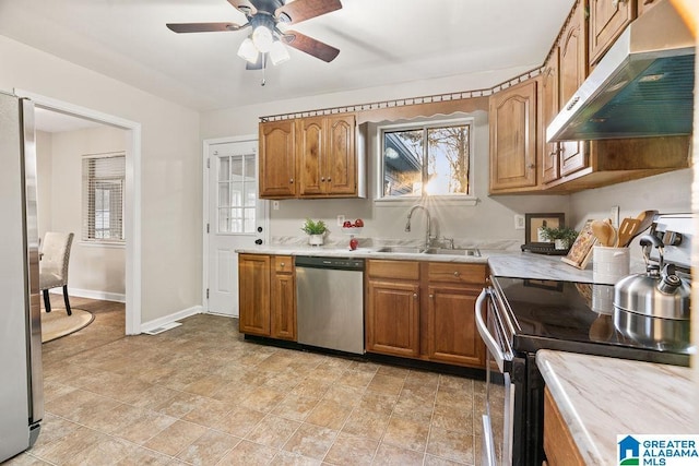 kitchen featuring under cabinet range hood, light countertops, brown cabinetry, stainless steel appliances, and a sink