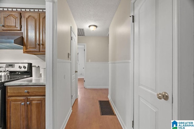 hallway featuring light wood-style flooring, wainscoting, visible vents, and a textured ceiling