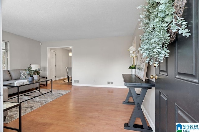 entryway featuring baseboards, visible vents, light wood-type flooring, and a textured ceiling