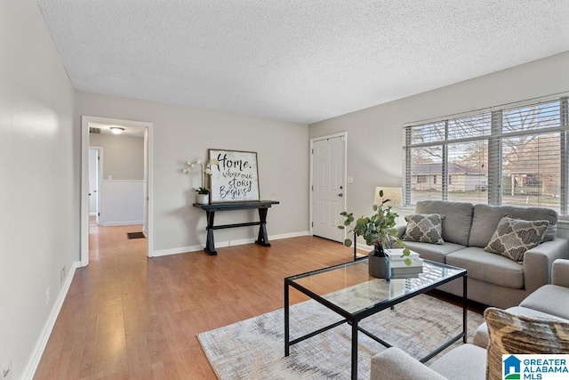 living room with baseboards, a textured ceiling, and light wood-style floors