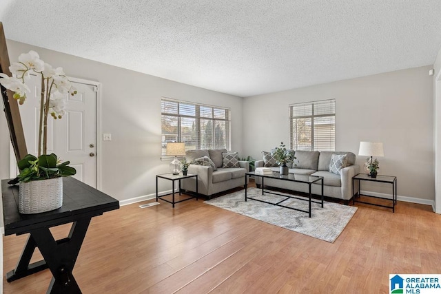 living area with visible vents, light wood-style flooring, a textured ceiling, and baseboards